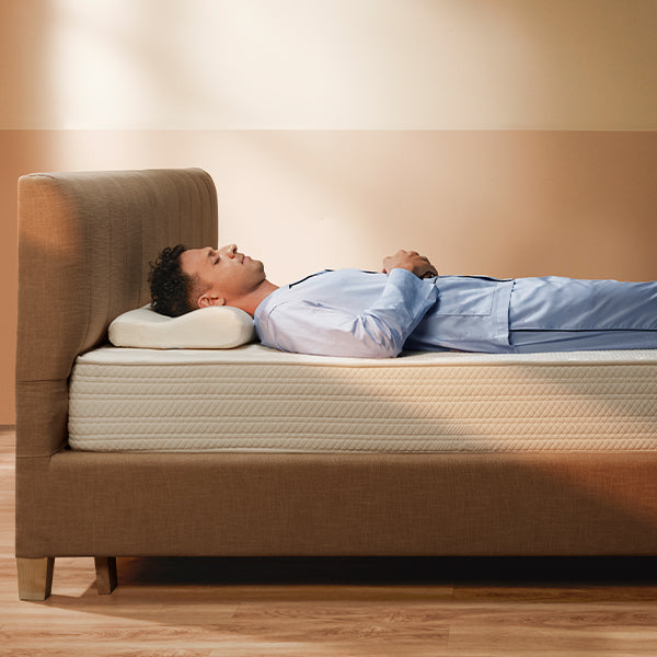 Man lying on a bed with a mattress and pillow, in a bedroom setting.