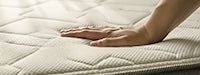 Hand touching a beige quilted mattress pad