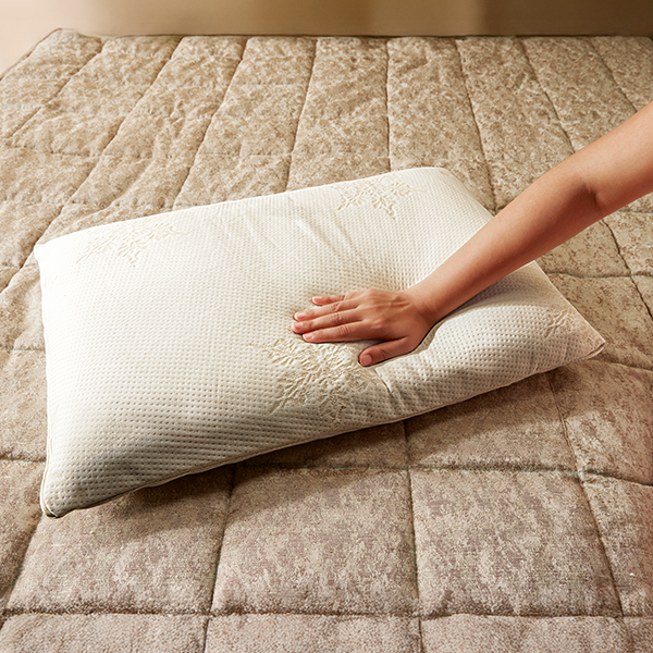 Hand touching a white pillow on a beige quilted bedspread