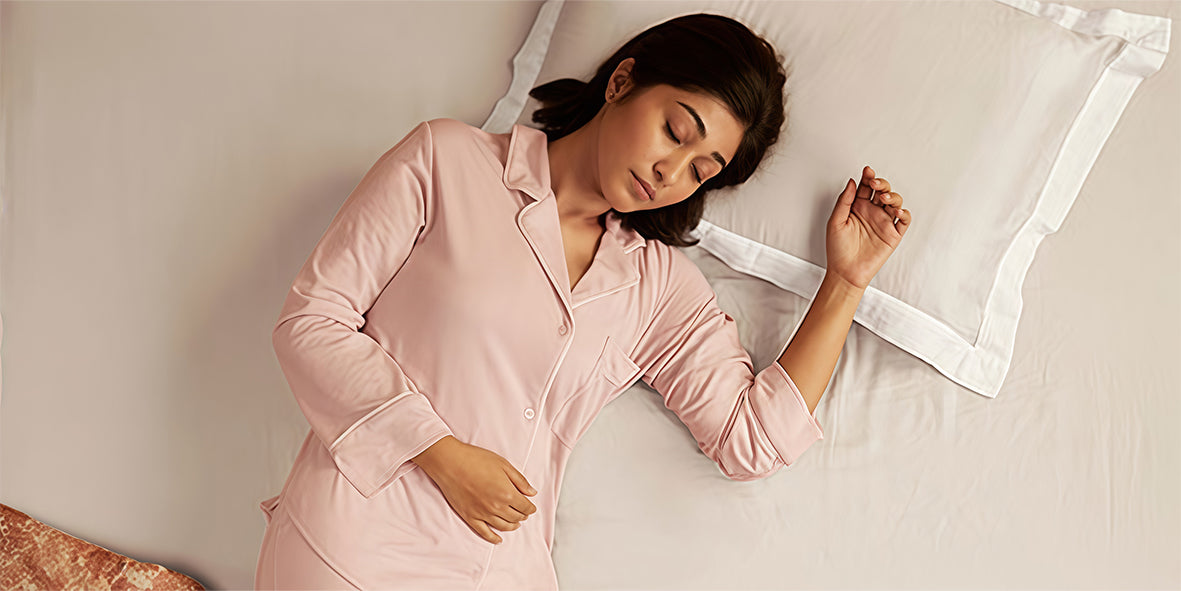 Woman in pink pajamas lying on a bed with a white pillow.