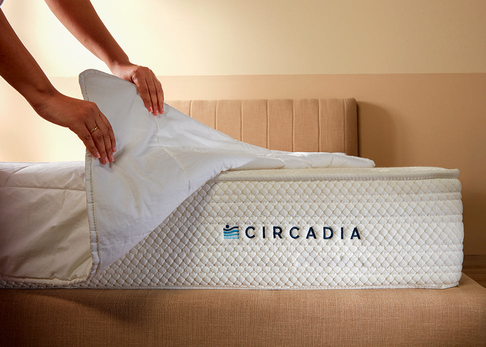 Person adjusting a mattress cover on a Circadia mattress in a bedroom setting.
