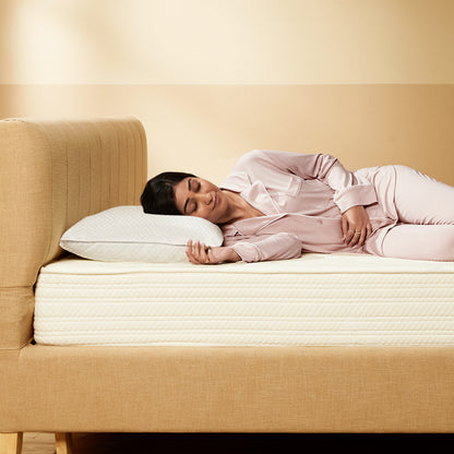 Woman lying on a mattress with a pillow, wearing pink pajamas, in a bedroom setting.