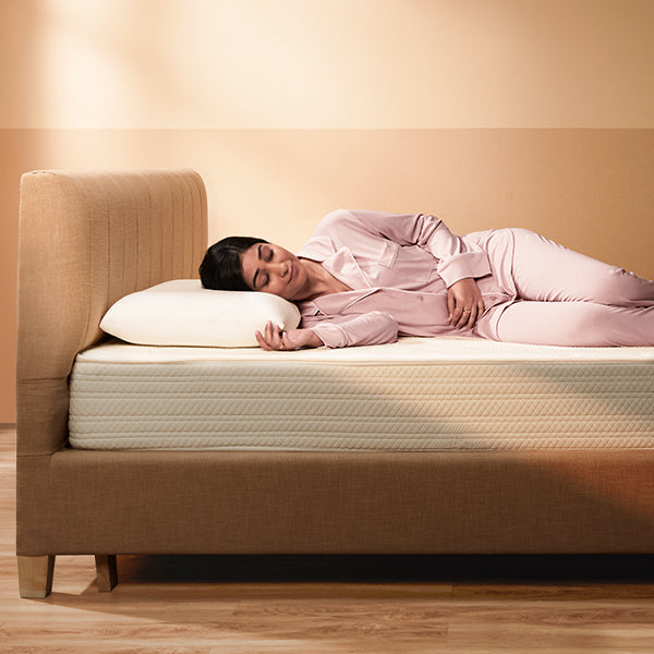 Woman lying on a bed with a beige mattress and headboard in a warm-toned room.