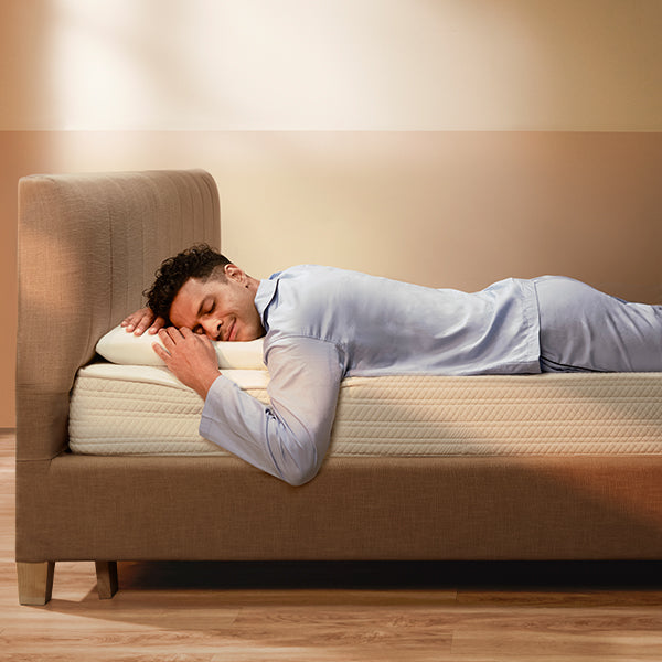 Man lying on a mattress in a room with beige walls and wooden floor.